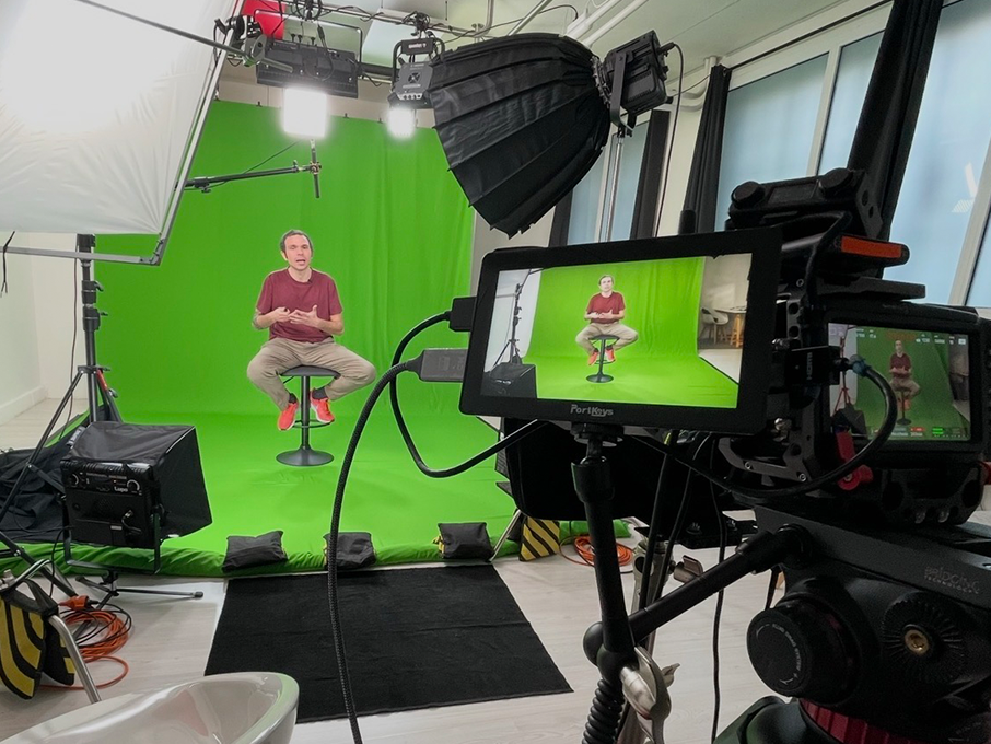 Intervista sul set: ospite seduto sul limbo verde durante una ripresa, con camera, monitor PortKeys e softbox in regia