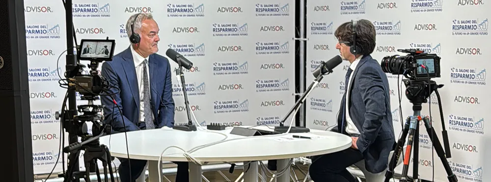 Intervista in regia durante un evento: due ospiti in cuffia al tavolo con camere su treppiede, microfoni a braccio e backdrop brandizzato