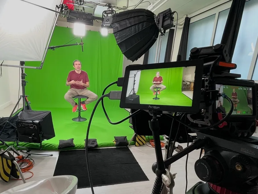Intervista sul set: ospite seduto sul limbo verde durante una ripresa, con camera, monitor PortKeys e softbox in regia